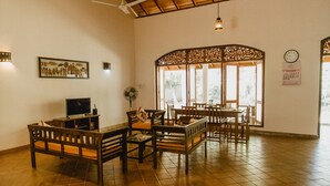 A spacious room with a high ceiling, a ceiling fan, a large window with decorative woodwork, and a wall-mounted clock.