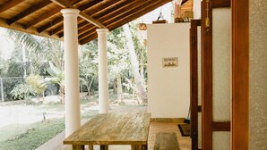 An outdoor covered patio with a wooden table and benches, white pillars, and a ceiling fan.