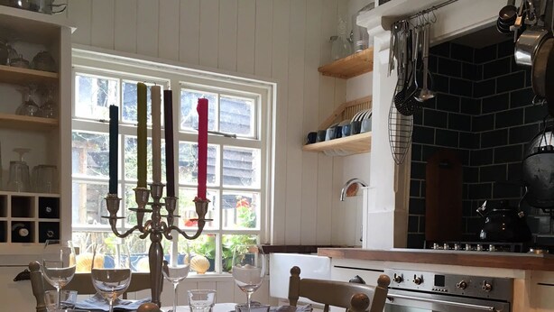 Una cocina con una mesa de madera, una silla blanca, un ventanal con vistas y una pared de ladrillo.