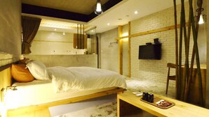 A modern bedroom with a wooden bed, a small wooden table, a TV mounted on a brick wall, and a large mirror. - Hotian Inn (Donggang)