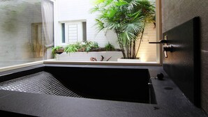 A modern bathroom with a black bathtub, a window, and a potted plant. - Hotian Inn (Donggang)