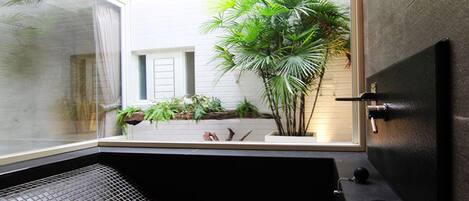 A modern bathroom with a black bathtub, a window, and a potted plant.
