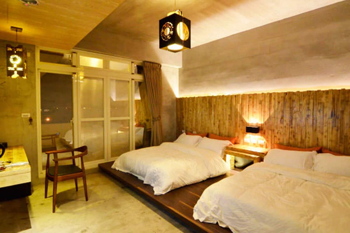 Habitación de hotel con dos camas, techo de madera y un ventanal grande con cortinas.