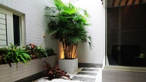 A courtyard with a white tiled wall, a potted plant, a wooden sculpture, and a pebble path. - Hotian Inn (Donggang)