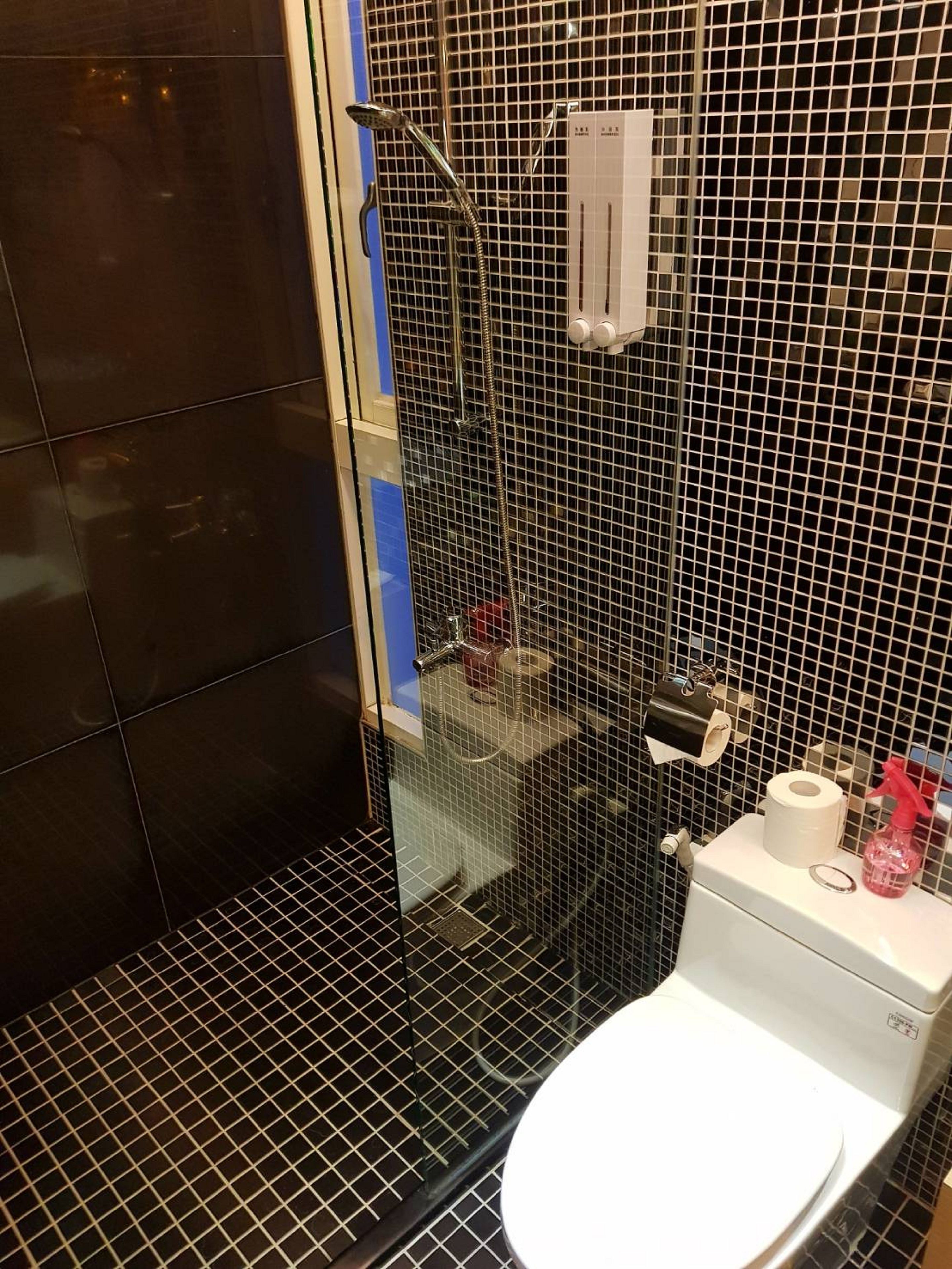 Une salle de bain avec une douche à parois de verre, des toilettes et une petite étagère contenant des articles de toilette.