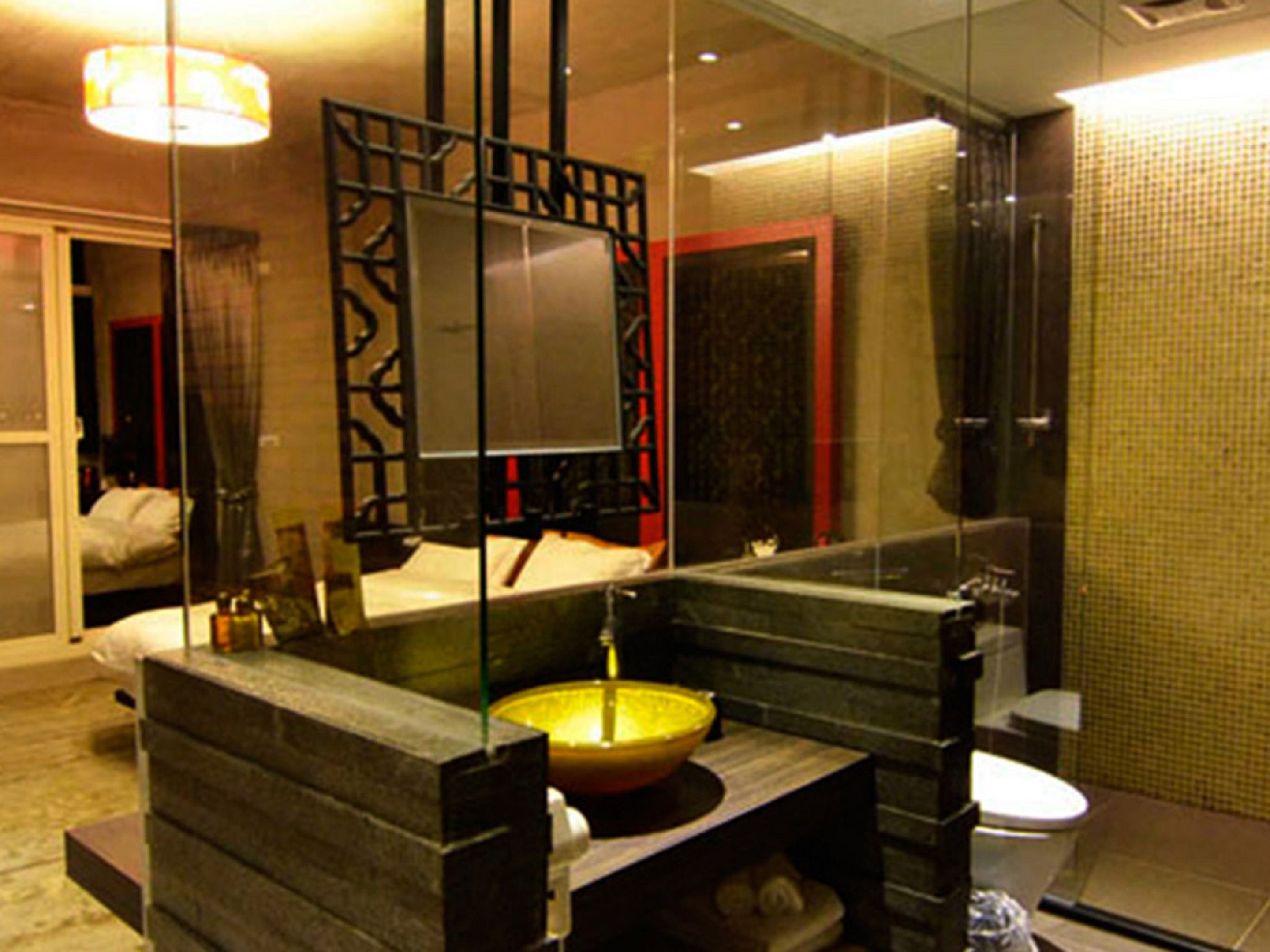 Een moderne badkamer met een glazen douchewand, een grote spiegel, een geel wastafel en een toilet.