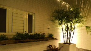 A white brick exterior with a window, a planter with a tree, and a stone pathway. - Hotian Inn (Donggang)