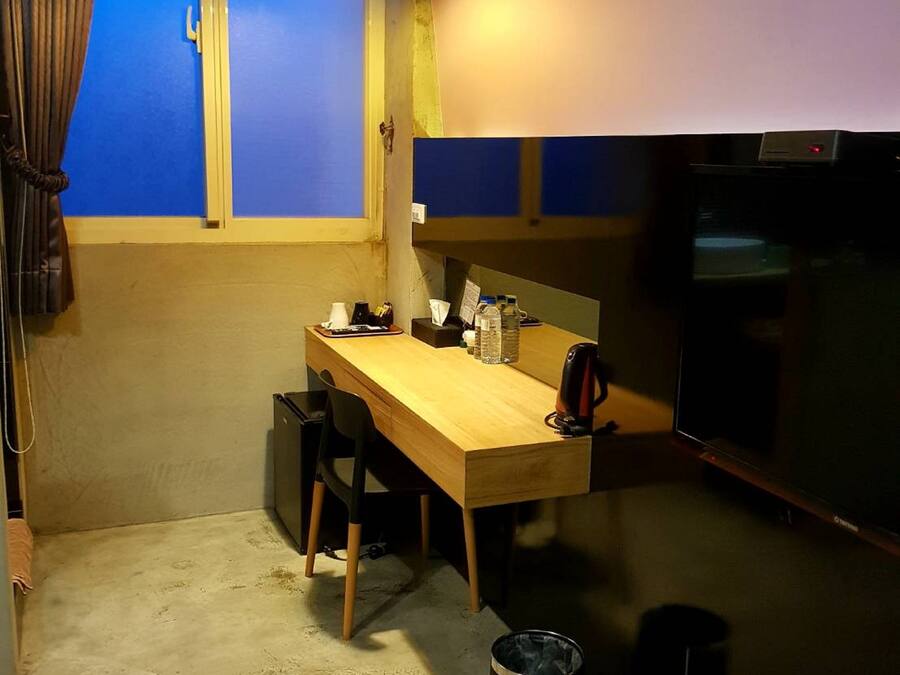 Una habitació petita amb taula de fusta, cadires, llum al sostre, finestra amb cortines i televisió.