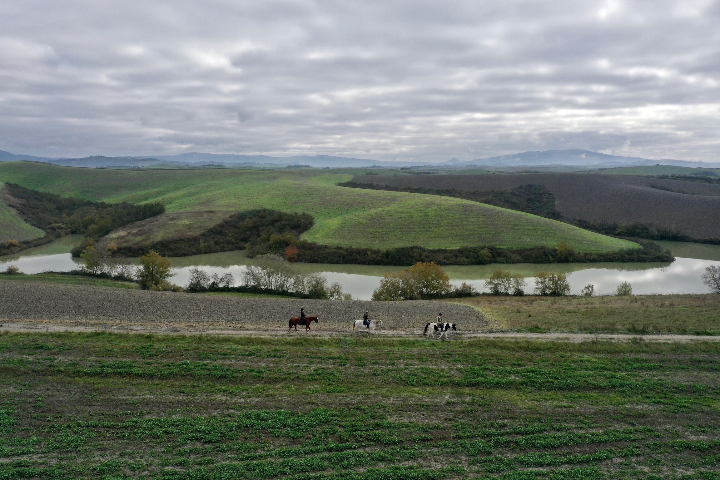 A landscape with rolling hills, a body of water, and a dirt path.