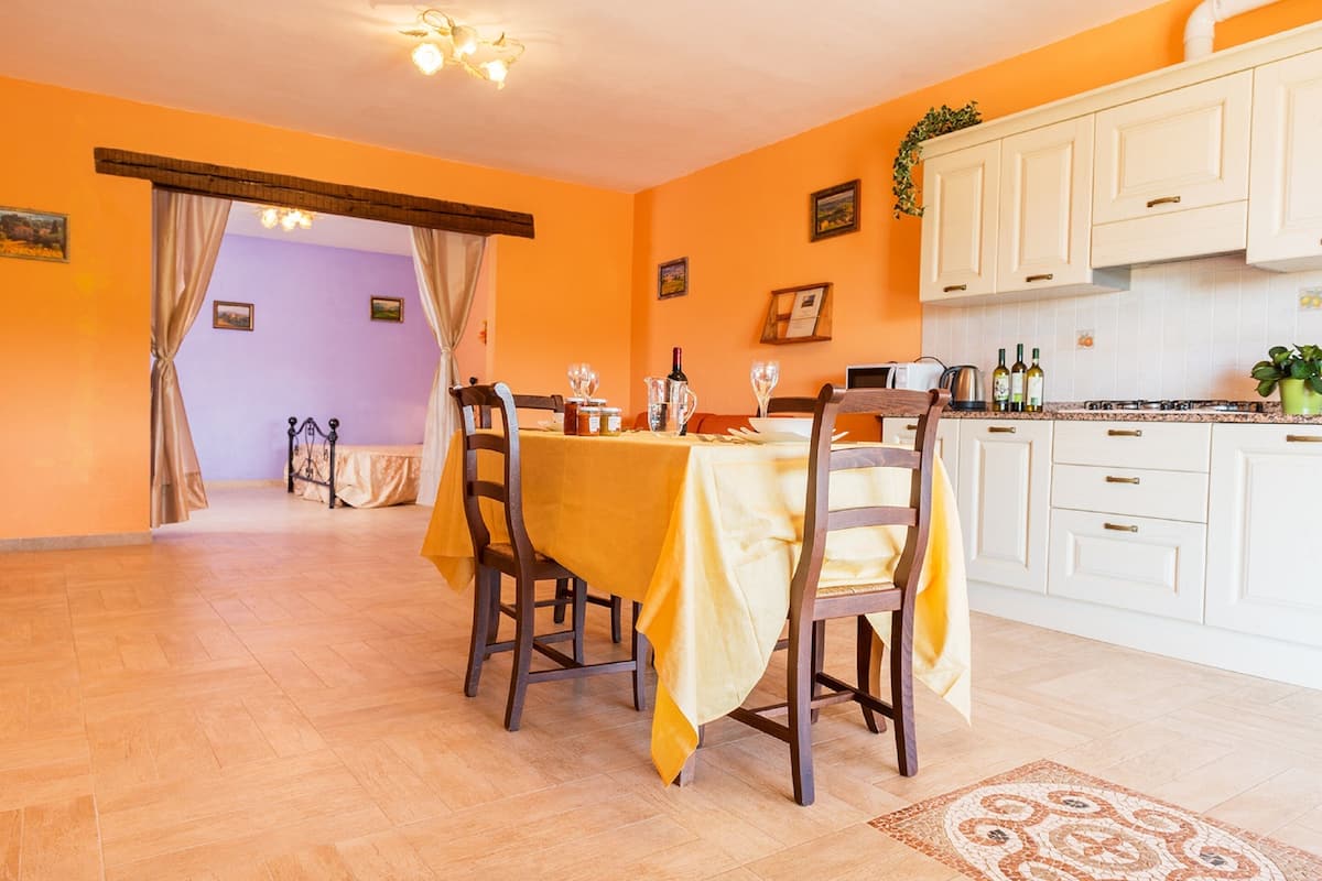 A dining area with a table set for four, a kitchen with white cabinets, and a view through a doorway to another room.