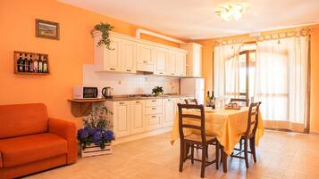 Una cocina luminosa con armarios blancos, una mesa de comedor con sillas y un sofá.