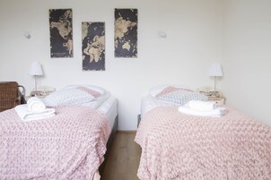 Habitación de hotel con dos camas, cada una con una manta rosa y una toalla enrollada. Dos mapas están colgados en la pared sobre las camas.