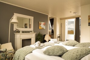 A hotel room with a bed, a fireplace, a mirror, a painting, and a view of the outside. - Private and peaceful one room apartments (Borgarnes)