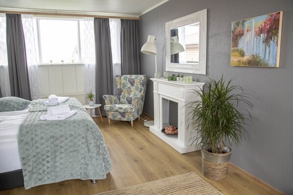 A hotel room with a bed, a chair, a small table, a mirror, a fireplace, and a potted plant. - Private and peaceful one room apartments (Borgarnes)