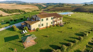 A two-story stone house with a swimming pool, surrounded by lush green fields and hills. - Agriturismo Panieracci (Volterra)