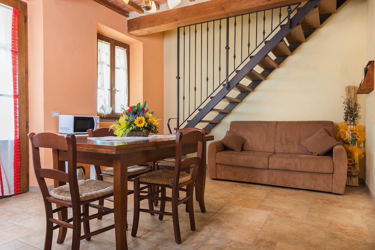 Uma área de refeições com uma mesa e cadeiras de madeira, um sofá e uma escada.