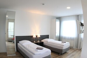 A hotel room with two beds, a large mirror, and a view of the outdoors through a window with curtains. - looks-inn (Viernheim)