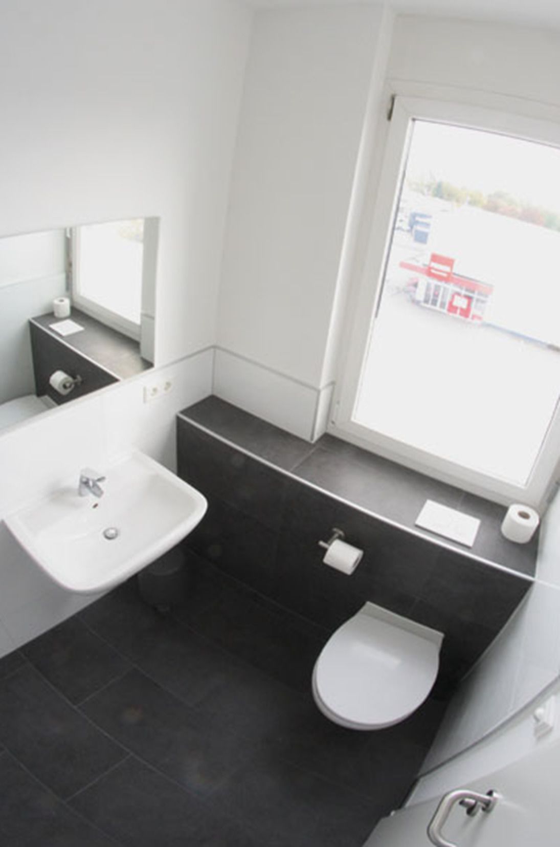 A modern bathroom with a white sink, a toilet, and a large window.