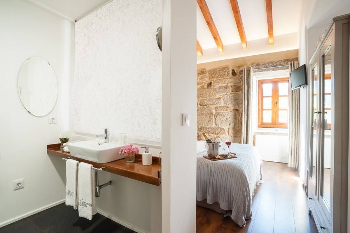 Un baño con lavamanos, espejo y barra para toallas. La habitación tiene una pared de piedra y un techo de madera.