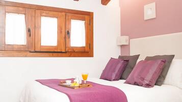 Un dormitorio con cama, vigas de madera, una ventana y una mesita de noche con bandeja.