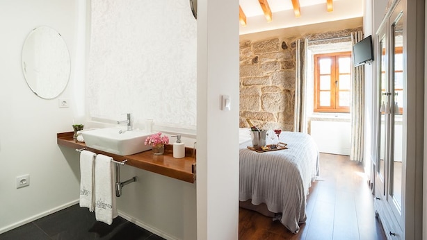 Un baño con lavamanos blanco, espejo y toallero. La habitación tiene una pared de piedra y techo de madera.