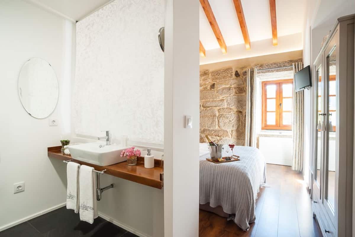 Un baño con lavamanos blanco, espejo y toallero. La habitación tiene una pared de piedra y techo de madera.