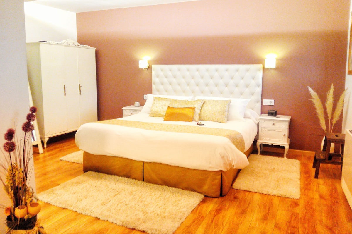 Un dormitorio ordenado con una cama grande, mesitas de noche, un armario y plantas decorativas.
