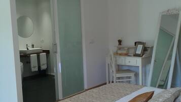 A bedroom with a bed, a dresser, a mirror, and a bathroom visible through an open door.