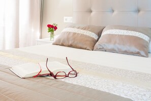 Una cama bien hecha con un libro y gafas encima, un florero con flores y una mesita de noche.