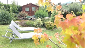 Un jardín con una cabaña de madera, una piscina y una silla de descanso blanca.