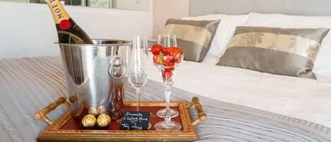 A bed with a champagne bottle, glasses, and chocolates on a tray.