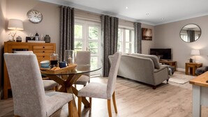 A modern living room with a glass dining table, grey sofas, and a flat-screen TV. - Durham Riverside Apartments (Durham)