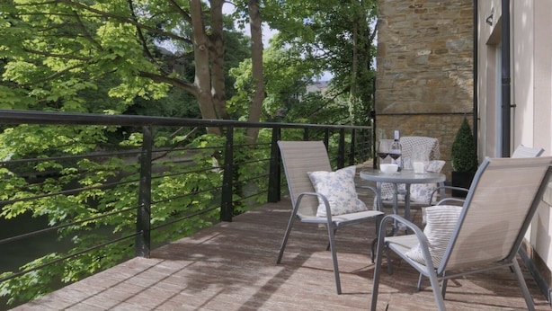A balcony with a stone wall, metal railing, and outdoor seating with chairs and a table. - Durham Riverside Apartments (Durham)
