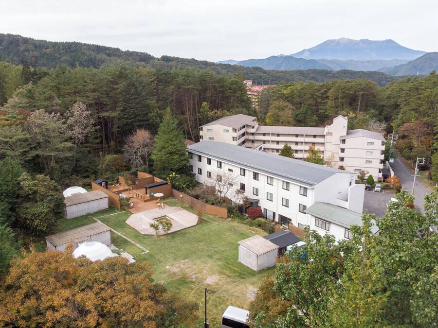 Un edificio de varios pisos con techo plano, rodeado de un césped cuidado y varias construcciones pequeñas.