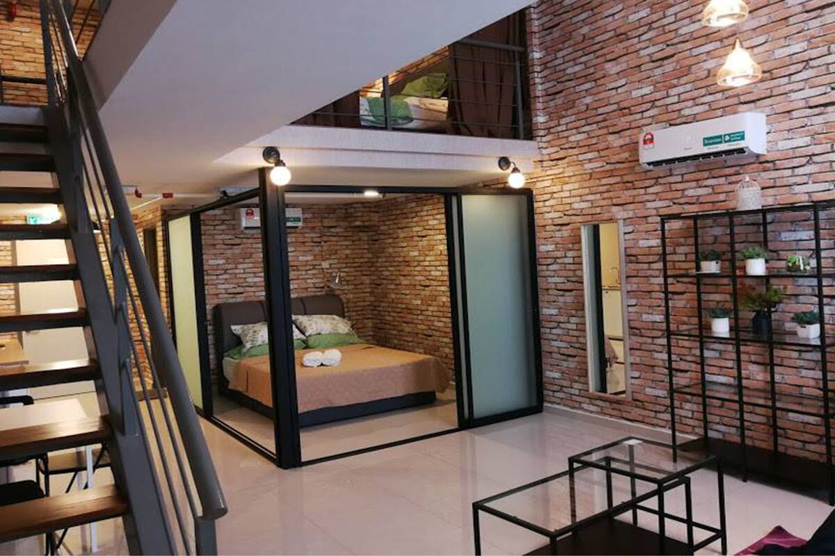 A modern interior with a loft-style bed, a staircase, and a brick wall with a built-in shelf.