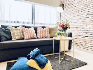 Un soggiorno moderno con un divano grigio, cuscini decorati, un tavolino rotondo con un vaso di fiori e una parete in mattoni.