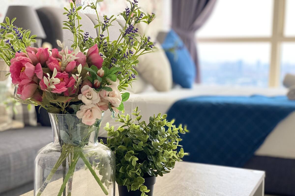A clear glass vase with pink and white flowers and a small potted green plant on a wooden table.