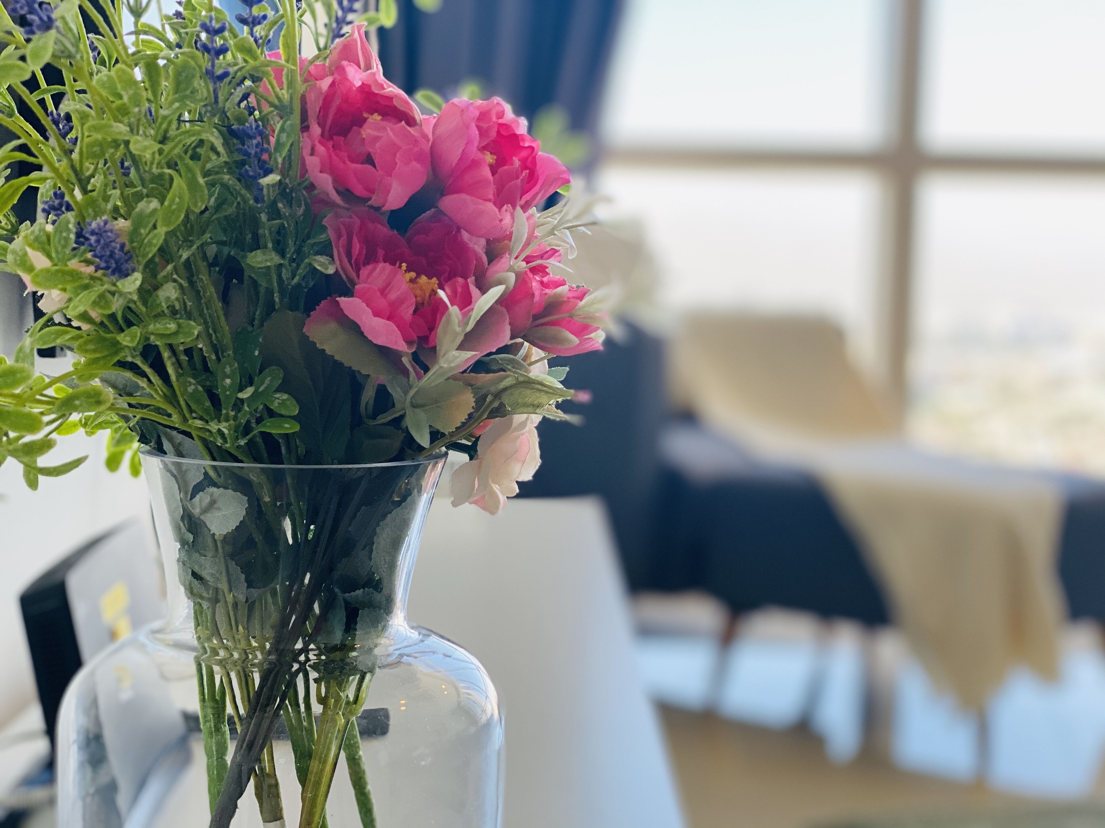 A clear glass vase with pink flowers and green foliage on a table.