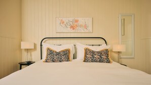 A hotel room with a bed, two pillows with a geometric pattern, a nightstand with a lamp, and a painting on the wall. - The Godolphin (Marazion)
