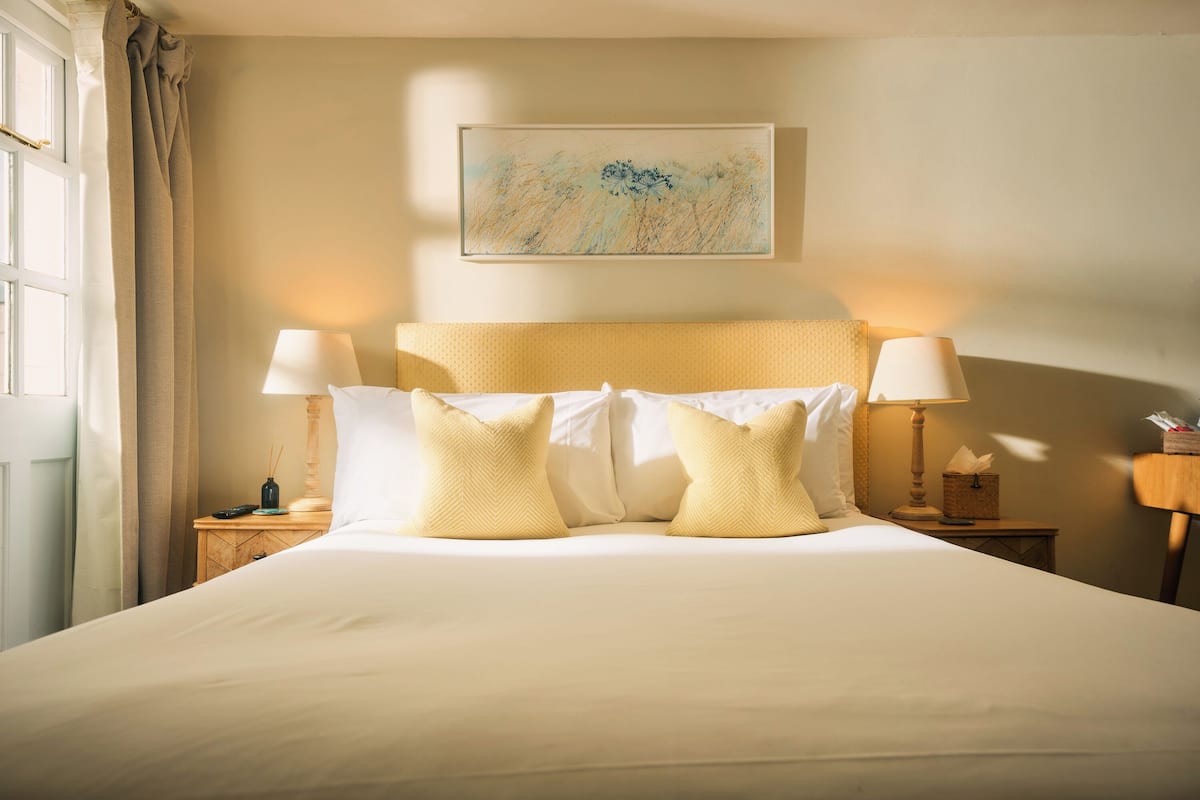 A neatly made bed with white and yellow pillows, a wooden headboard, and two bedside lamps.