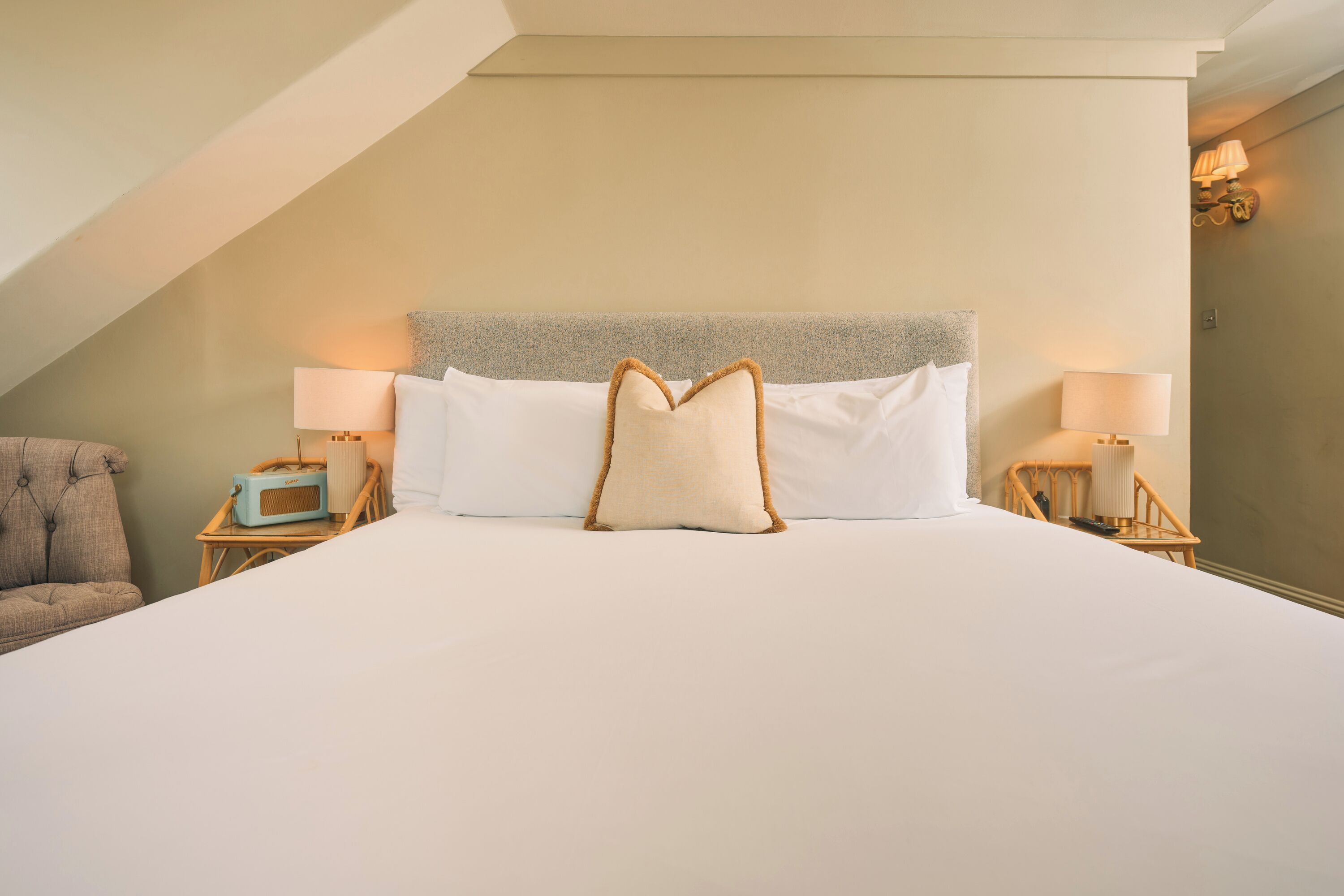 Una habitación de hotel con una cama grande, dos lámparas de noche, una silla y una radio.