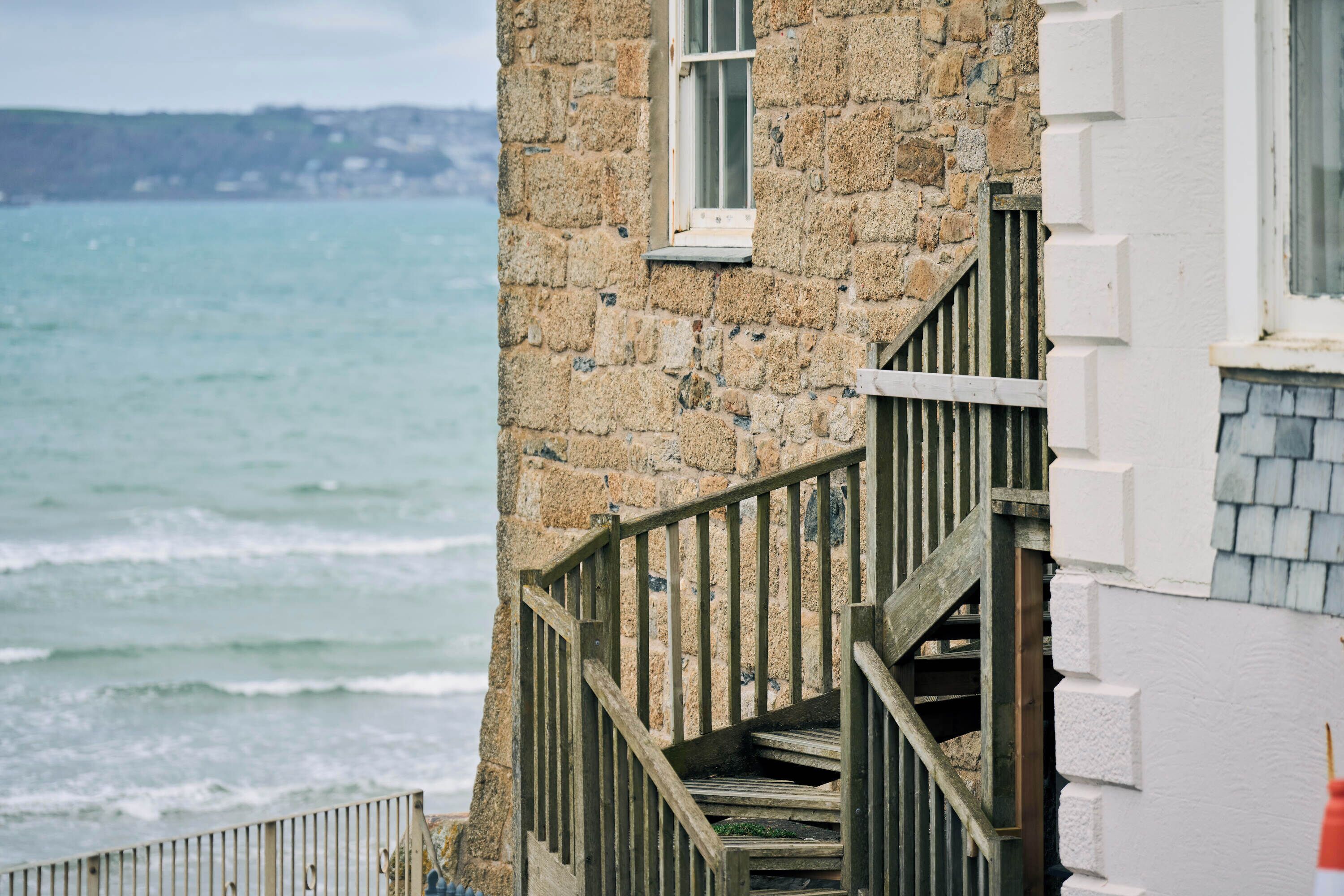 A stone building with a wooden staircase leading to a window overlooking the sea.