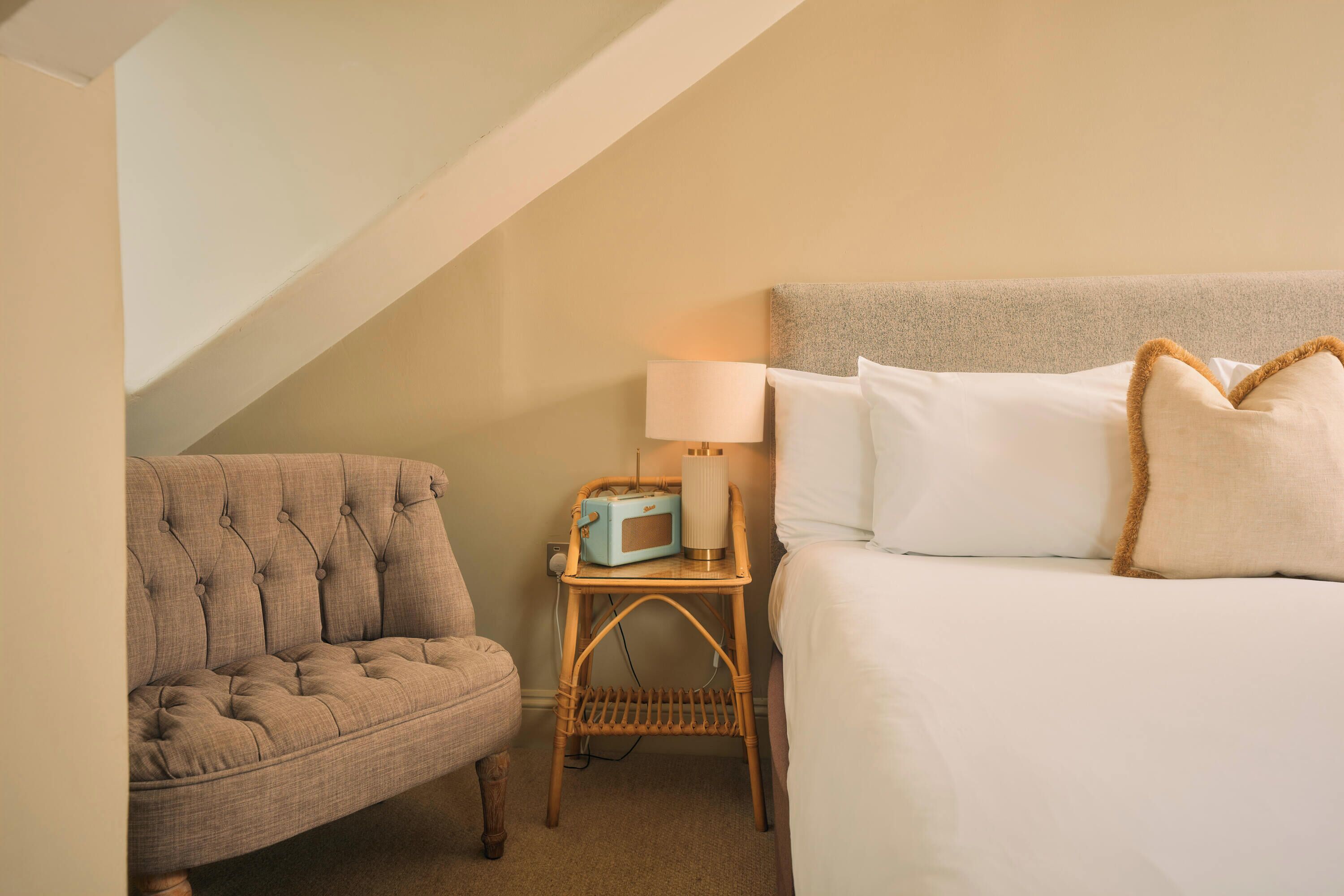 A bedroom with a bed, a chair, a nightstand, and a lamp.