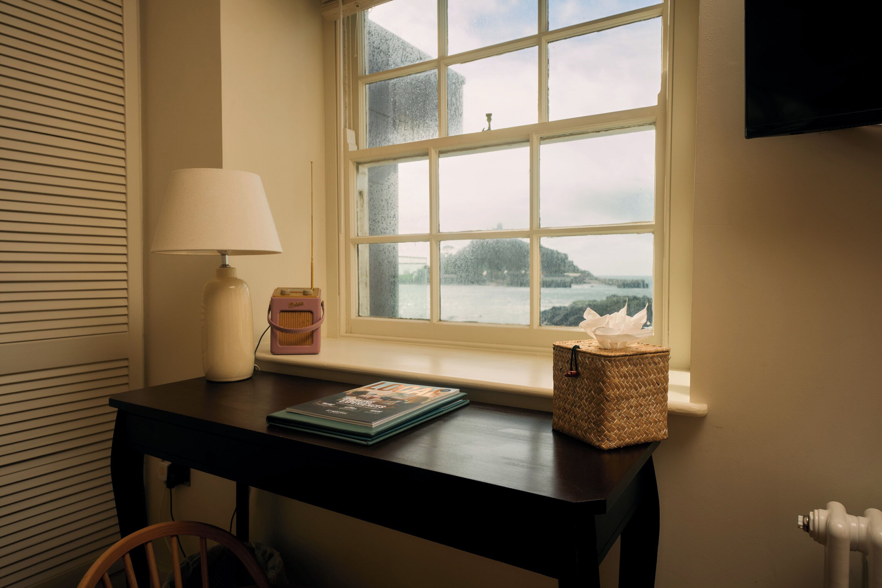 A room with a window, a table, a lamp, a basket, and a magazine.