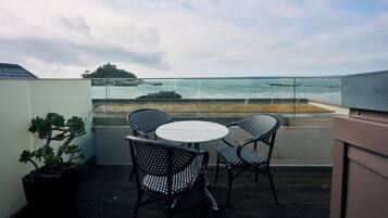 A balcony with a round table and two chairs, overlooking a coastal view with a castle on a hill and rocky outcrops in the water.