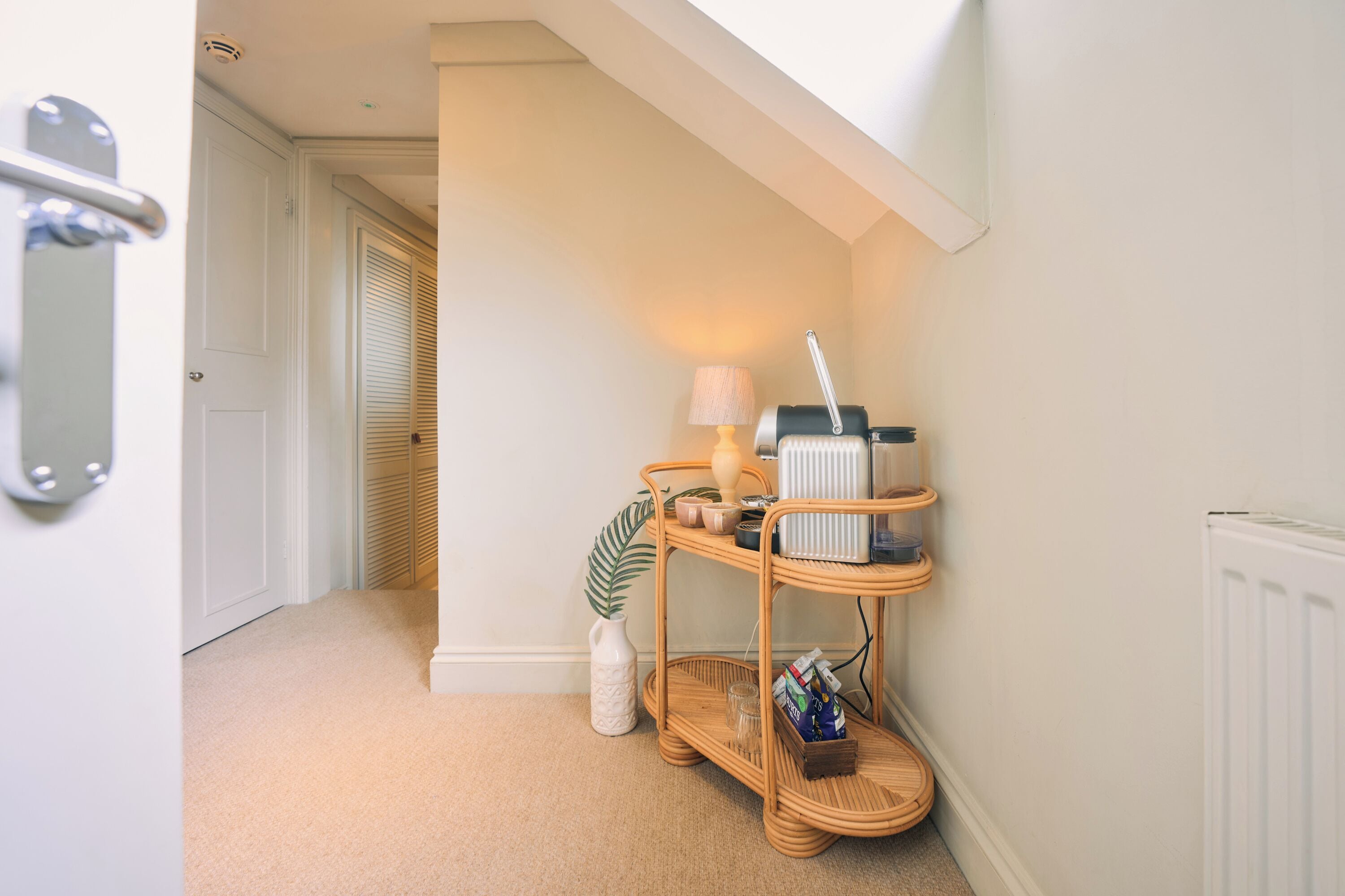 A hallway with a white door, a radiator, a wicker shelf with various items, and a lamp.