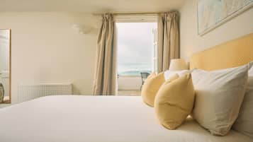 A hotel room with a bed, a window with curtains, a lamp, and a view of the sea.