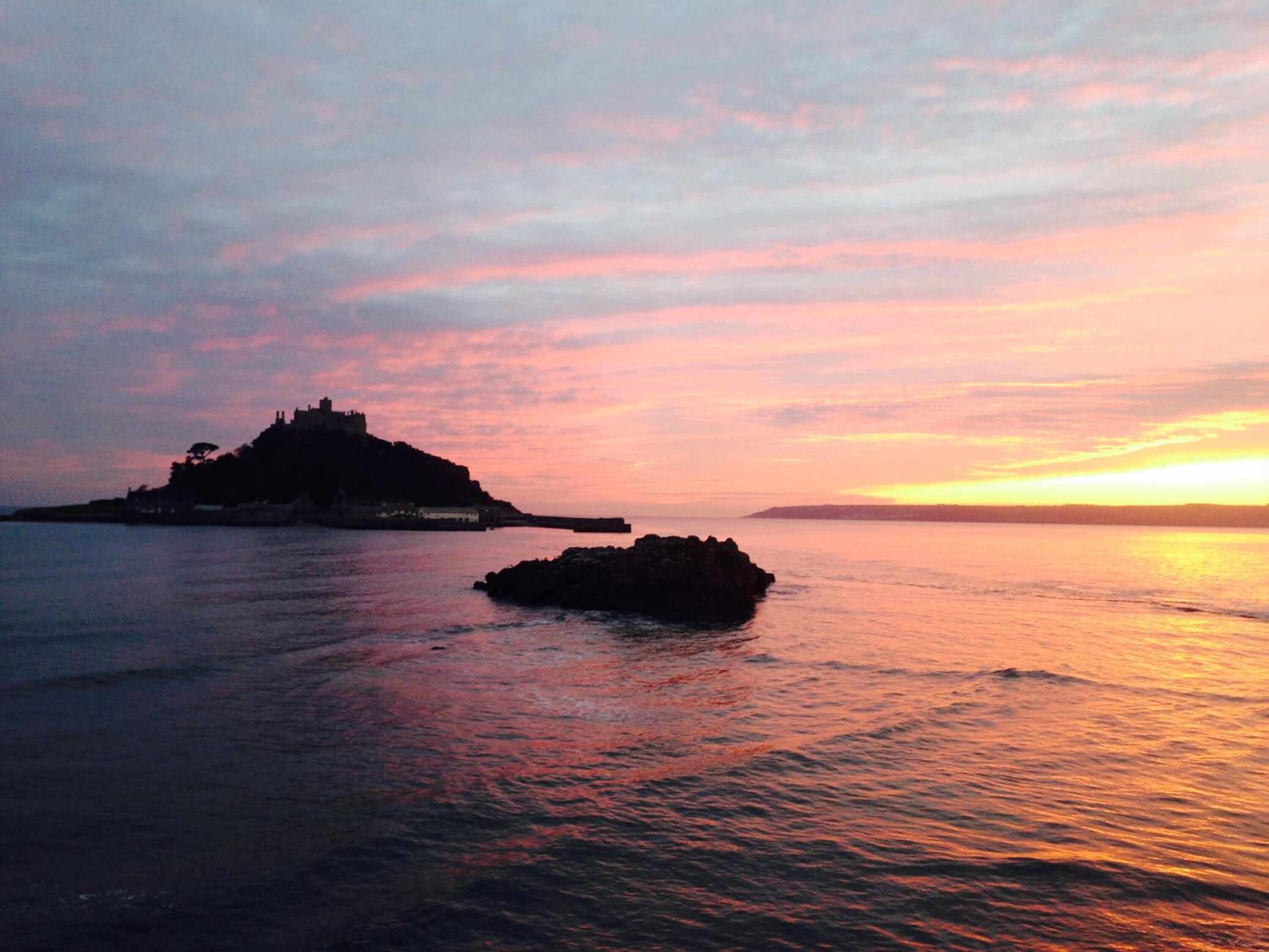 A coastal scene with a prominent hilltop structure and a small rock formation in the water.