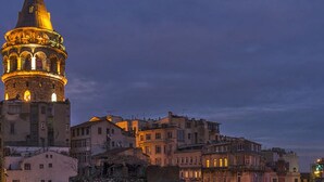A historic tower with illuminated windows, surrounded by buildings with varied architectural styles.