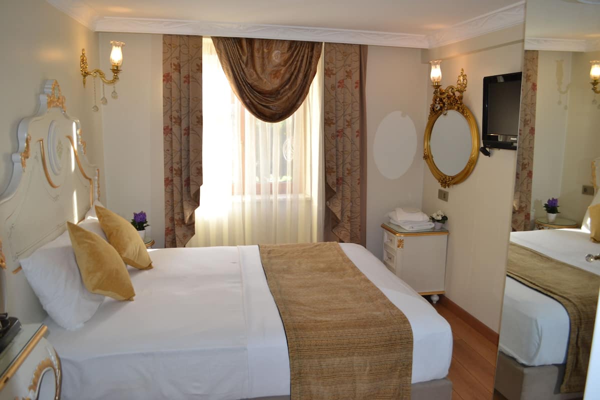 A hotel room with a large bed, a bedside table with a lamp, a mirror, and a window with curtains.